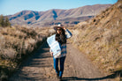 Girl walking down path in the high desert with blue blanket on her shoulder