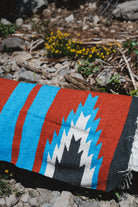 blue and red relampago design handwoven zapotec blanket laying on a log