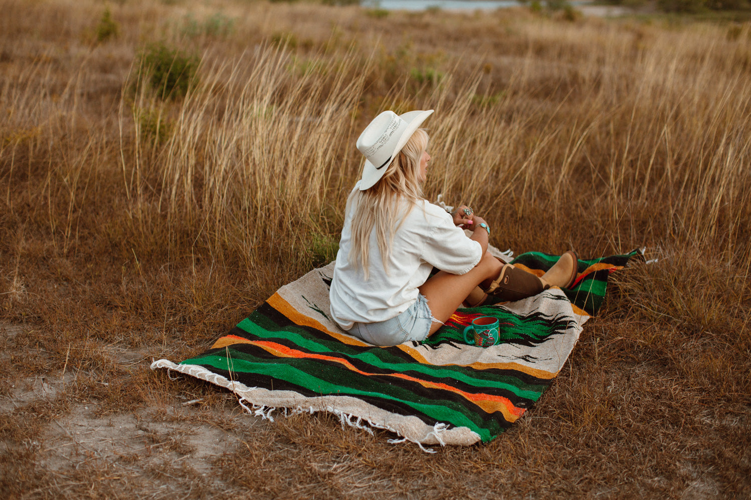 girl sitting on diamond blanket in a tall field of dry grass