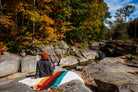 Girl sitting on rocky creekside on top of colorful blanket