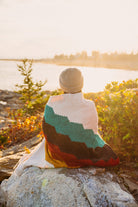 Girl sitting on rock wrapped in blanket at sunset