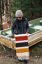 Girl wearing grey beanie and holding striped blanket in front of a boat