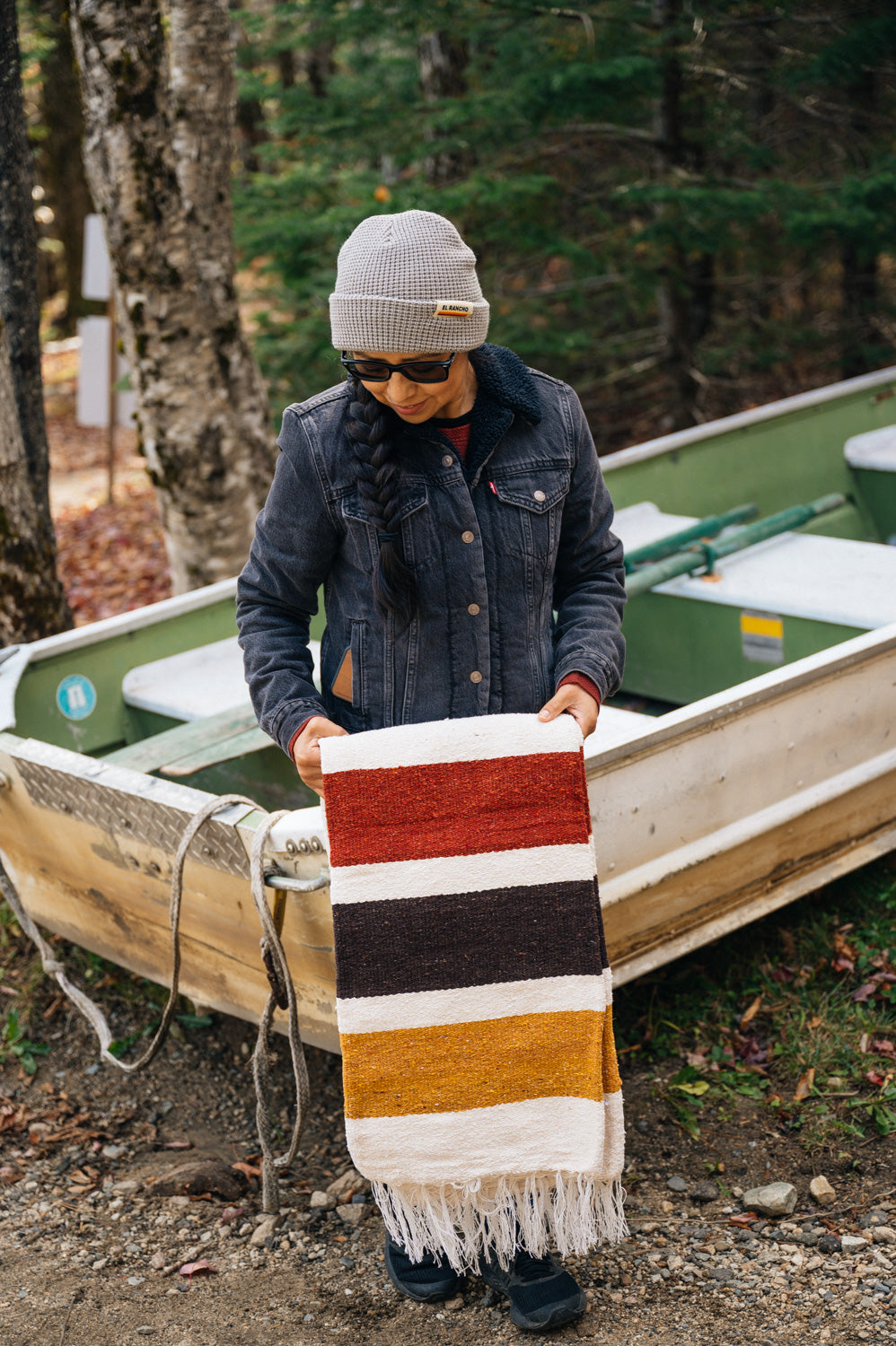 Girl wearing grey beanie and holding striped blanket in front of a boat