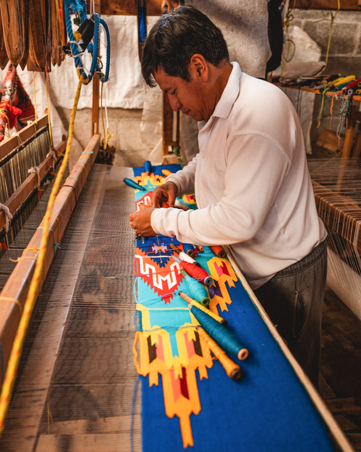 Mexican man hand weaving intricate blanket on a wooden loom