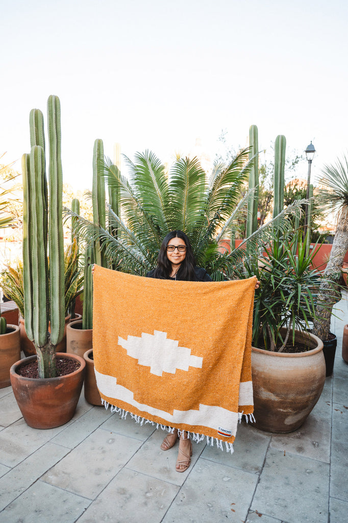 Mixtec woman holding handwoven serape in front of cactus garden on patio in Oaxaca