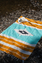 Turquoise, gold and white handowoven mexican blanket laying on a rocky riverbank