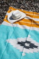 Turquoise, gold and white handowoven mexican blanket laying on a rocky riverbank