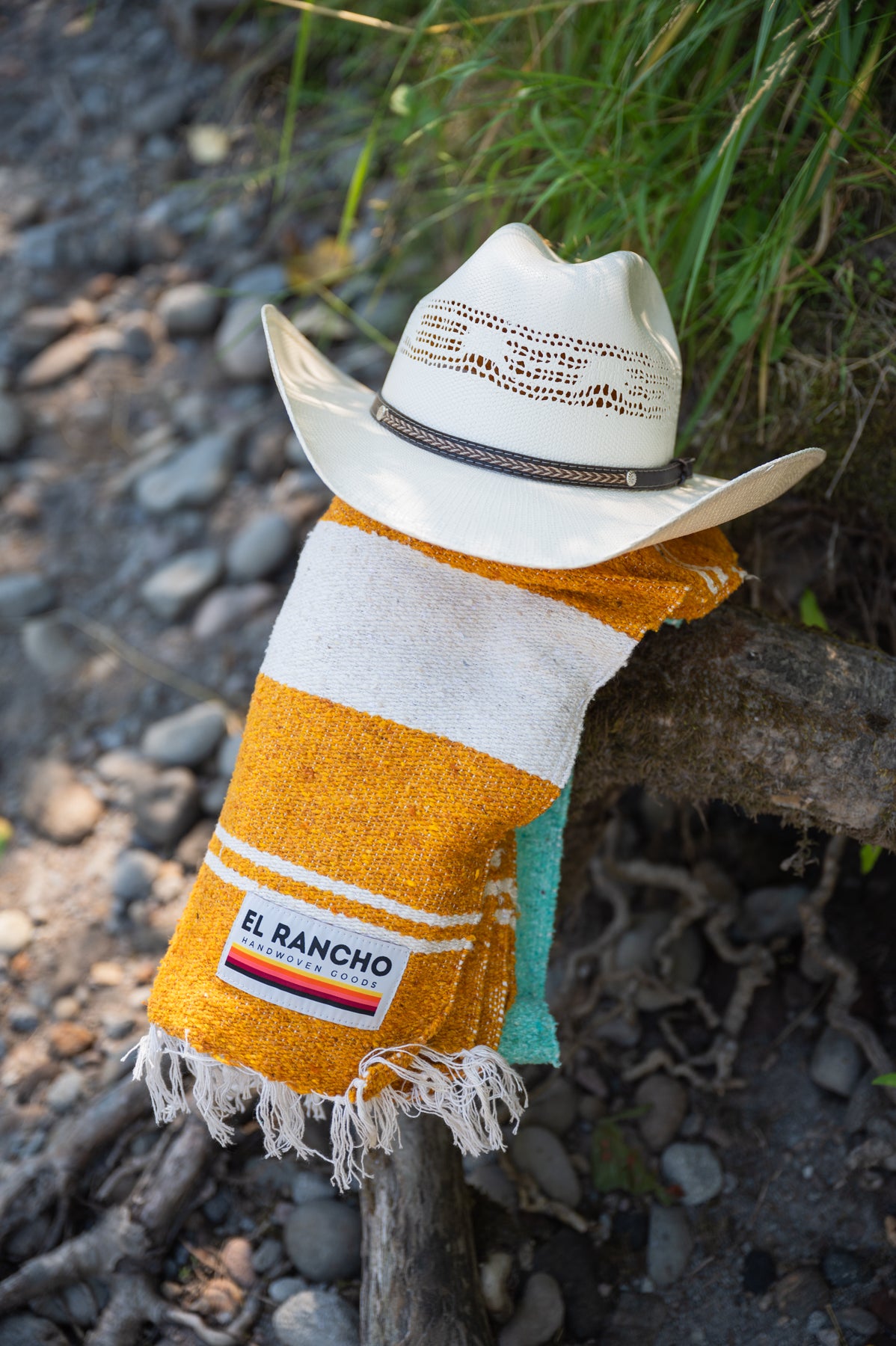 Turquoise, gold and white handowoven mexican blanket laying on a rocky riverbank