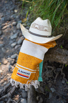 Turquoise, gold and white handowoven mexican blanket laying on a rocky riverbank