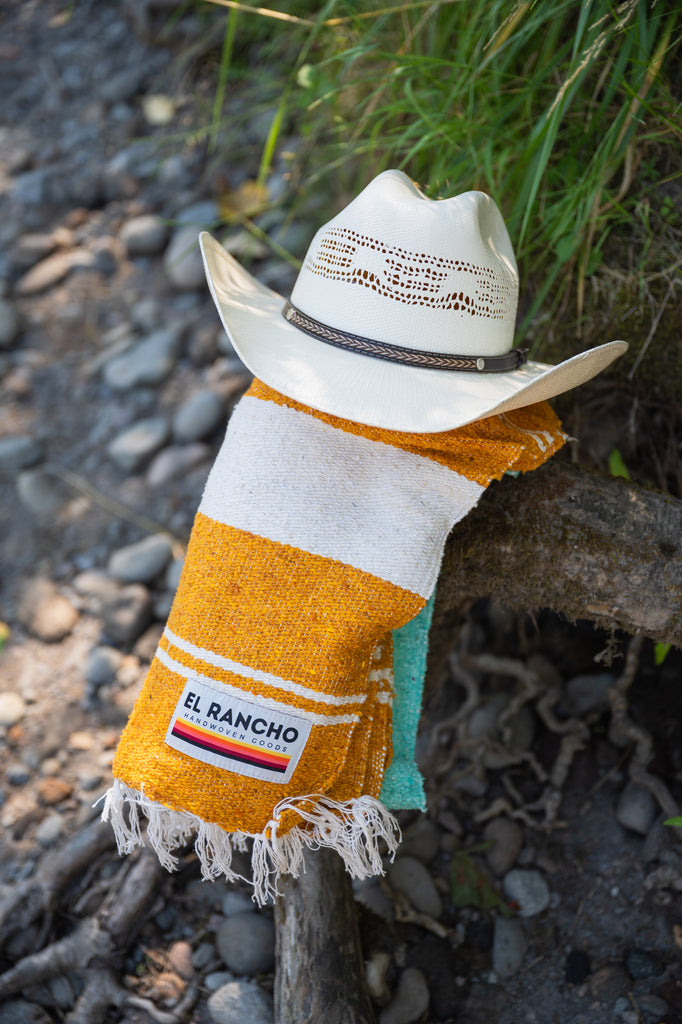 Turquoise, gold and white handowoven mexican blanket laying on a rocky riverbank