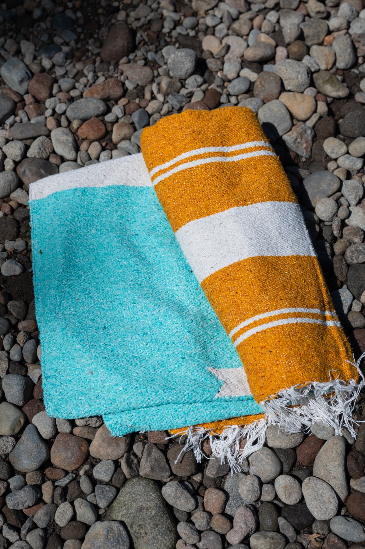 Turquoise, gold and white handowoven mexican blanket laying on a rocky riverbank