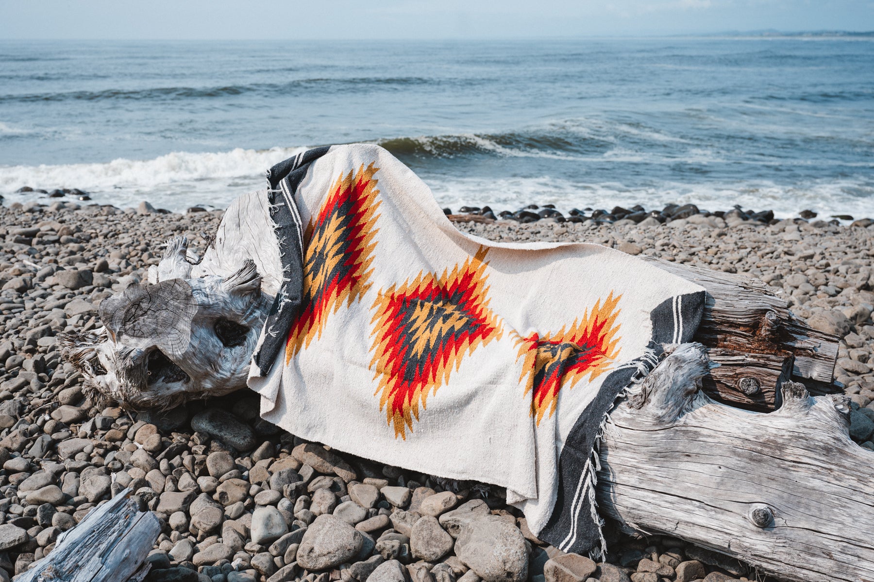 red and black southwest diamond sarape laying on log at beach