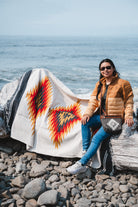 girl sitting on red and black southwest style handwoven diamond sarape at the beach 