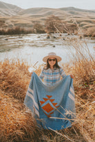 woman holding blue handwoven blanket in the high desert by a river