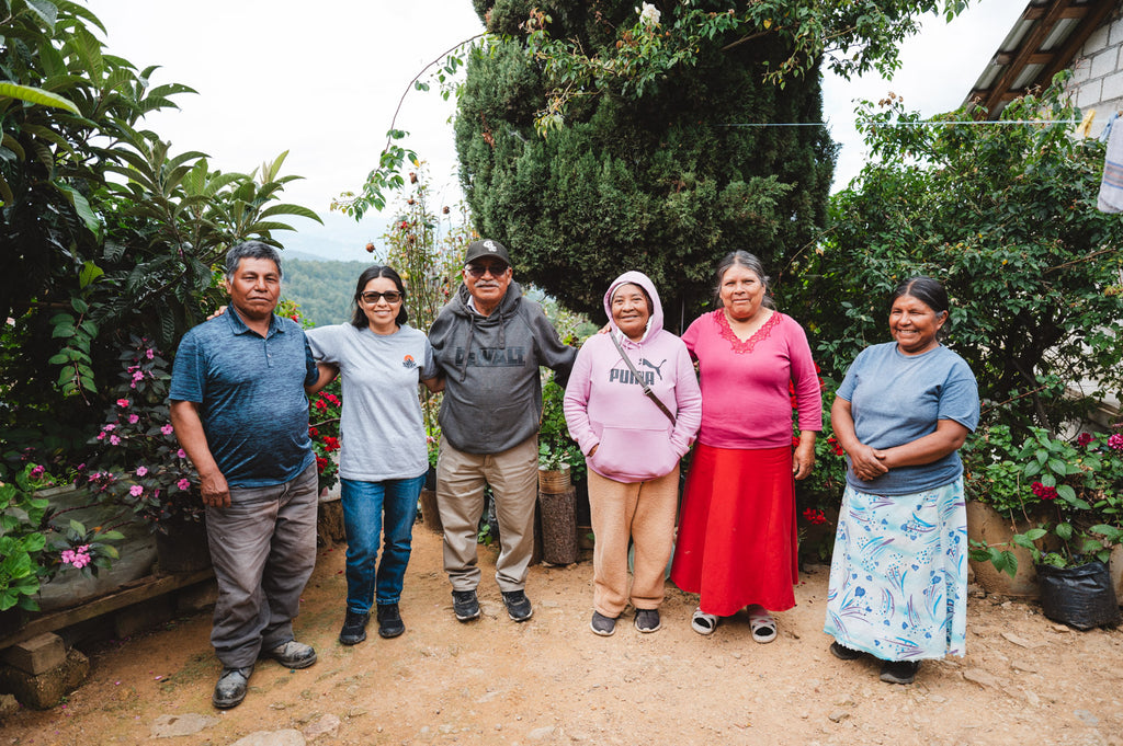 Family of 6 indigenous Mixtec people posing for a photo standing side by side in front of bushes and trees