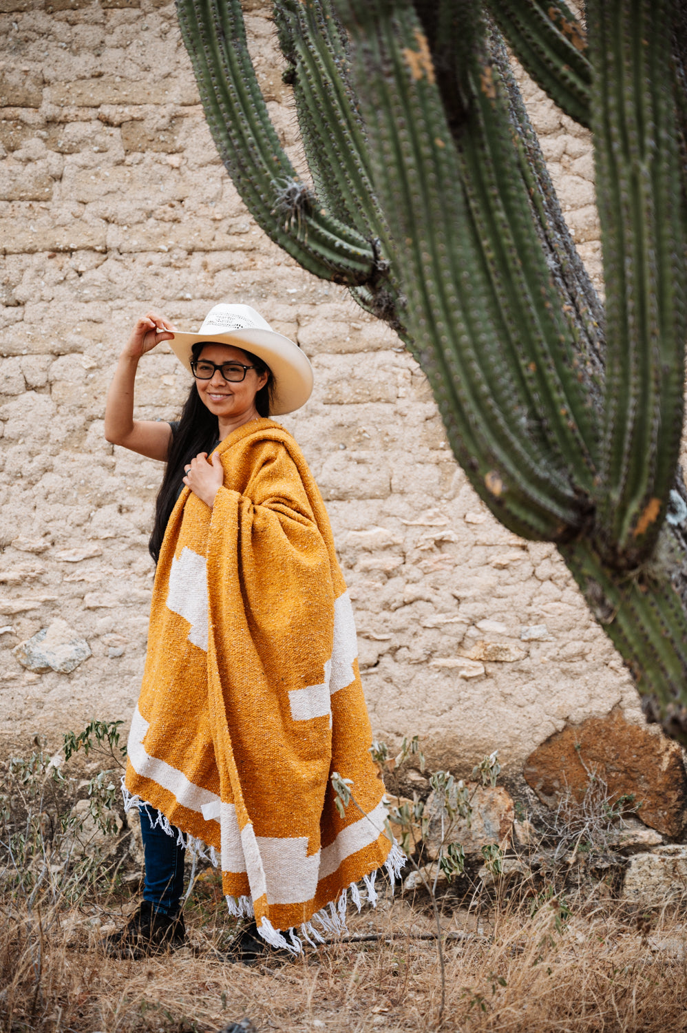 Girl wrapped in orange blanket in front of a cactus in Oaxaca