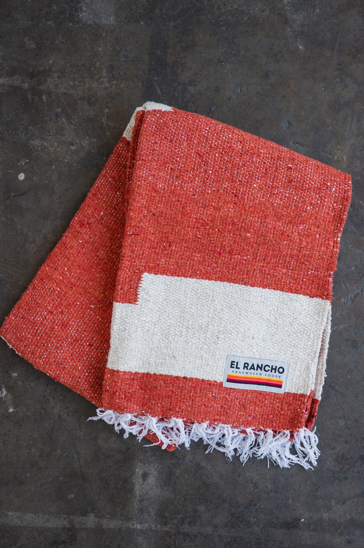 Red handwoven throw blanket folded laying on concrete floor