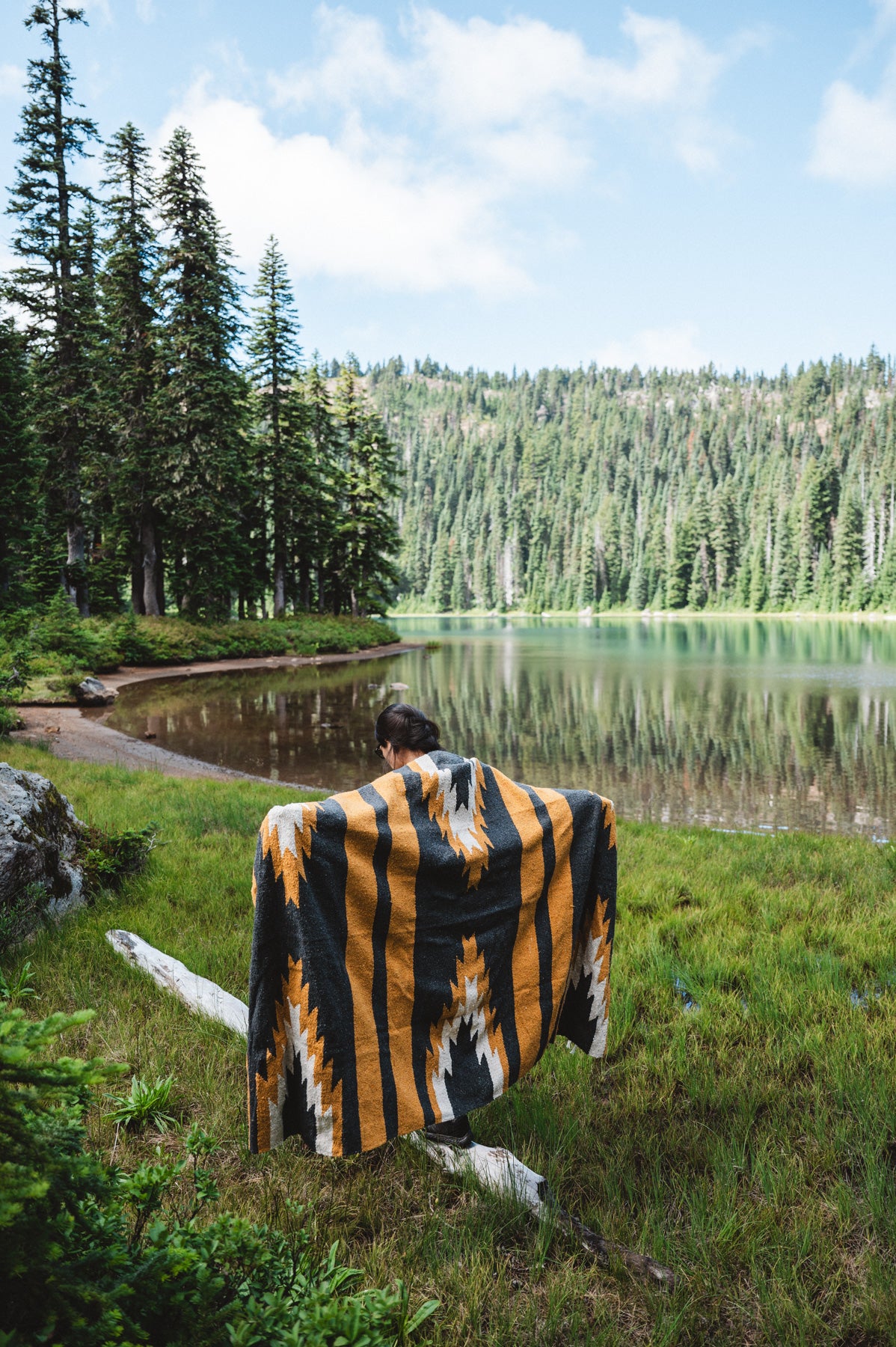 Girl wearing black and yellow zapotec handwoven mexican blanket in front of alpine lake