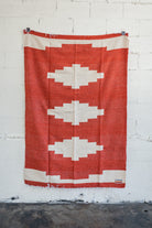 Red diamond handwoven Mexican Blanket hanging on white brick wall