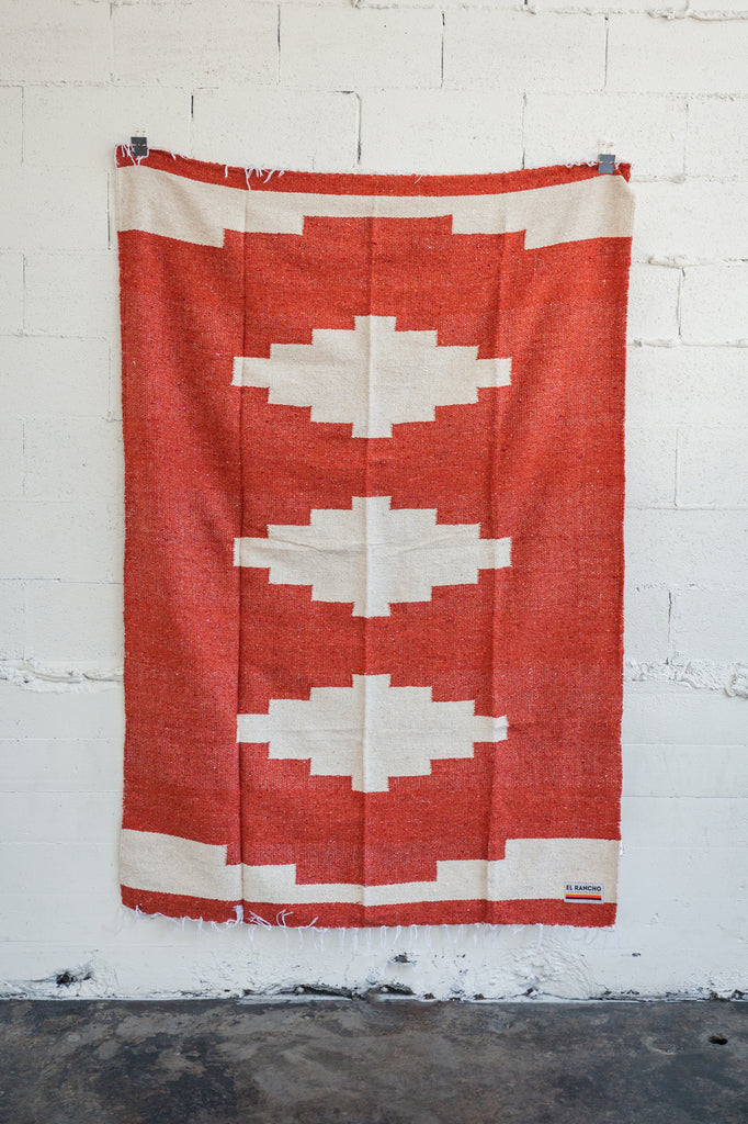 Red diamond handwoven Mexican Blanket hanging on white brick wall