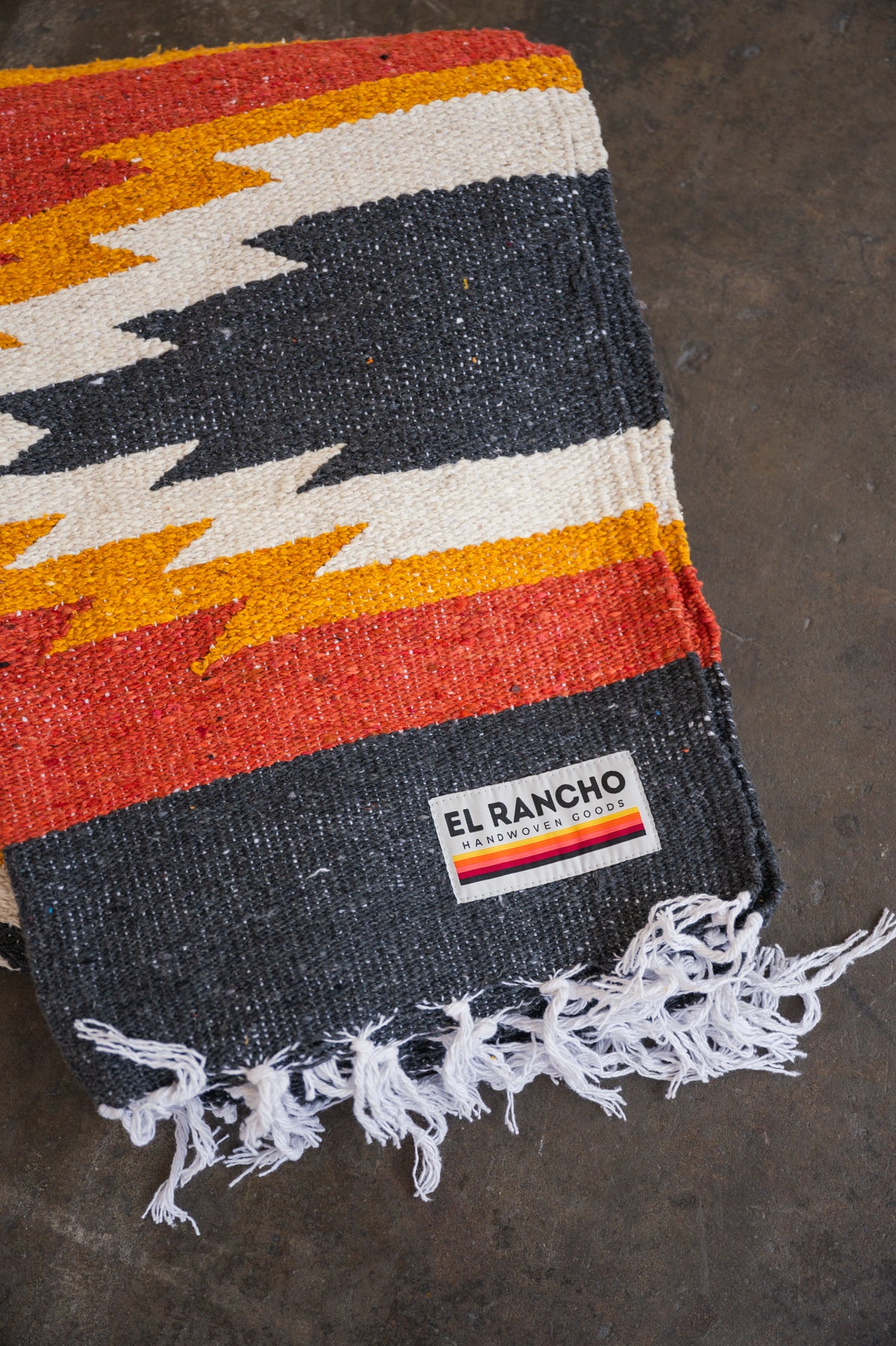 red and yellow mexican blanket laying folded on concrete floor