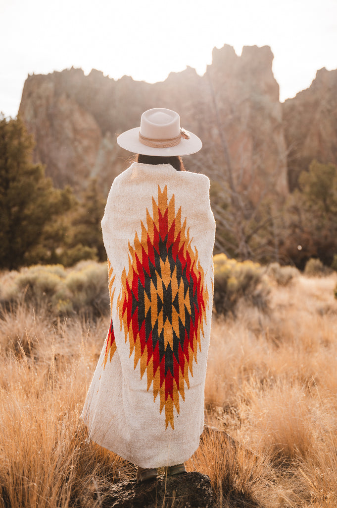 Woman wearing cowboy hat wrapped in southwestern style diamond blanket in the desert