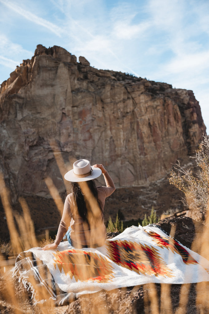 Woman sitting on southwestern style blanket in the desert wearing a cowboy hat