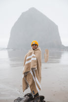 Woman wrapped in tan handwoven blanket in front of Haystack Rock Cannon Beach