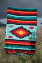 Teal and red handwoven mexican blanket being held up in a field