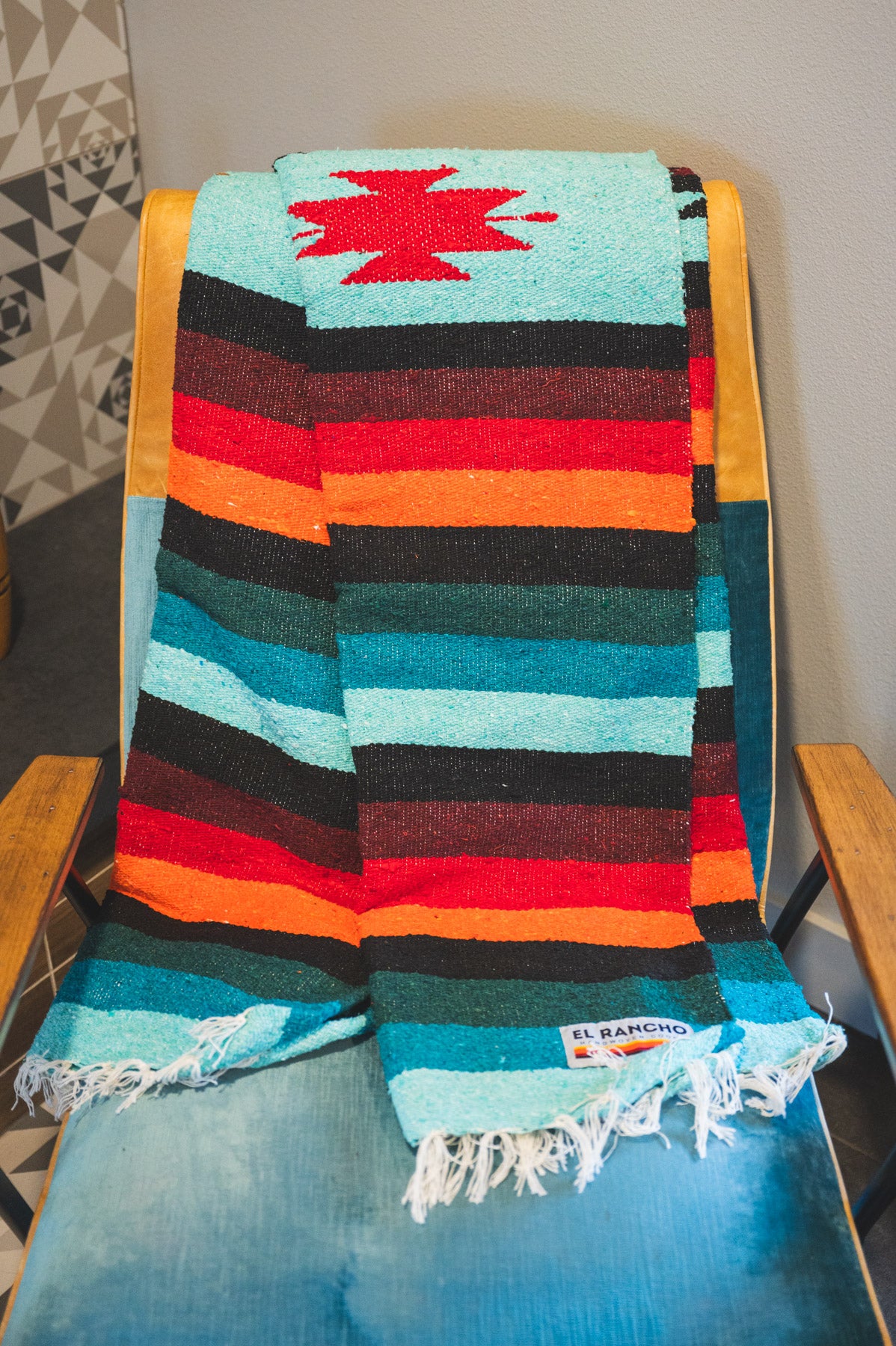 Teal and orange handwoven diamond zapatec blanket laying on a chair in a living room