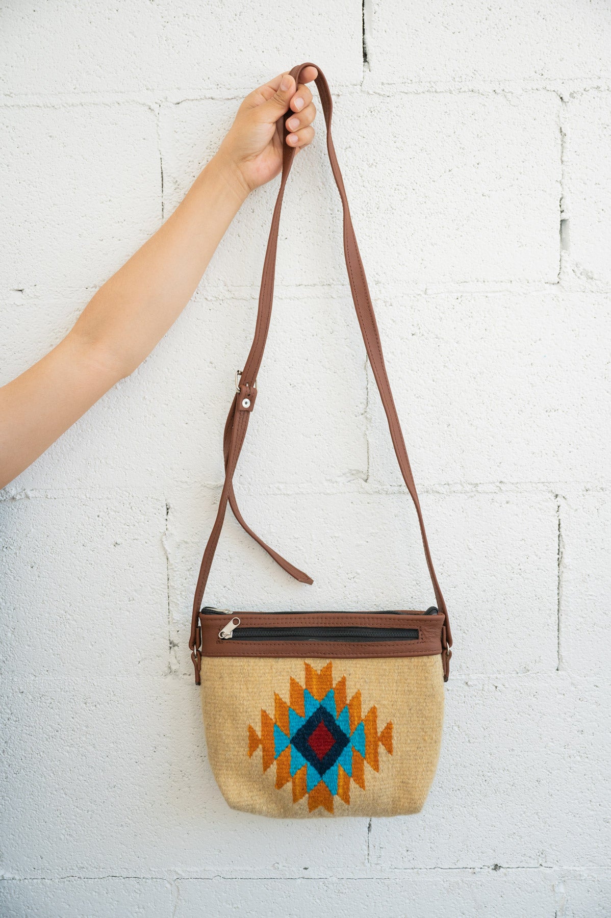 Gold and blue Mexican handbag being held against a white brick wall by an arm