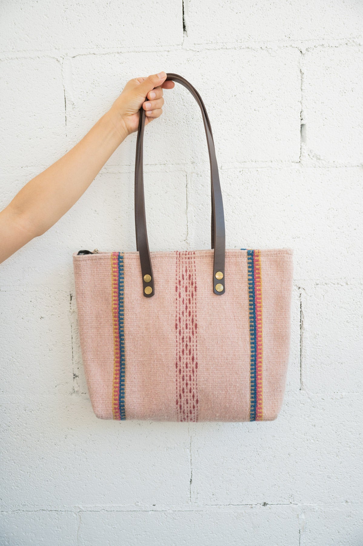 Pink Mexican handbag being held against a white brick wall by an arm