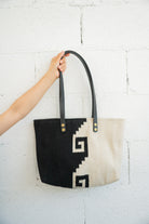 Black and white Mitla design Mexican handbag being held against a white brick wall by an arm