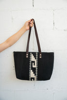 Mitla designed black and white Mexican handbag being held against a white brick wall by an arm