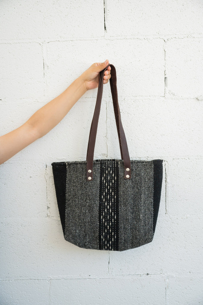 Black and grey handwoven Mexican purse being held against a white brick wall by an arm