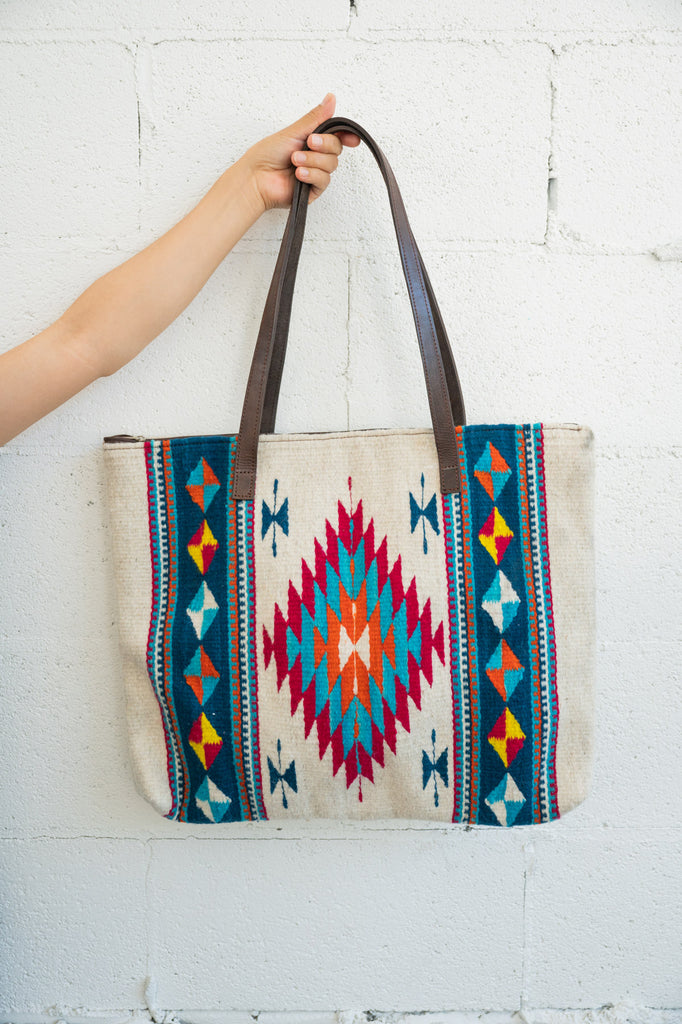 Mexican handbag being held up by an arm against a white brick wall