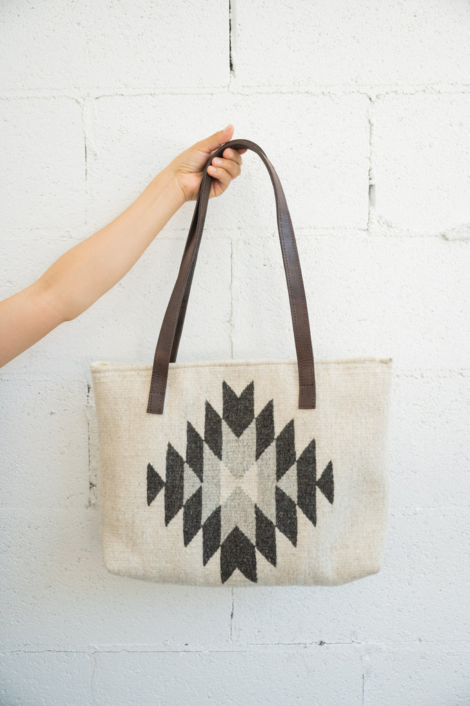 Creme and grey Mexican handbag being held up by an arm against a white brick wall