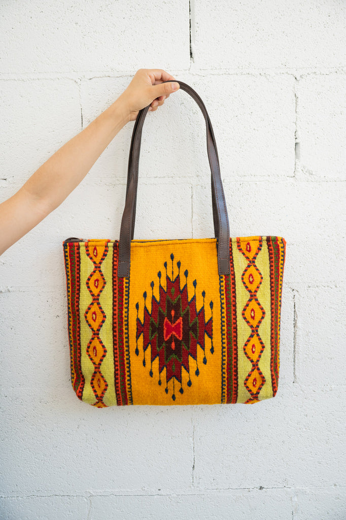 Orange and yellow Mexican purse being held against a white brick wall by an arm