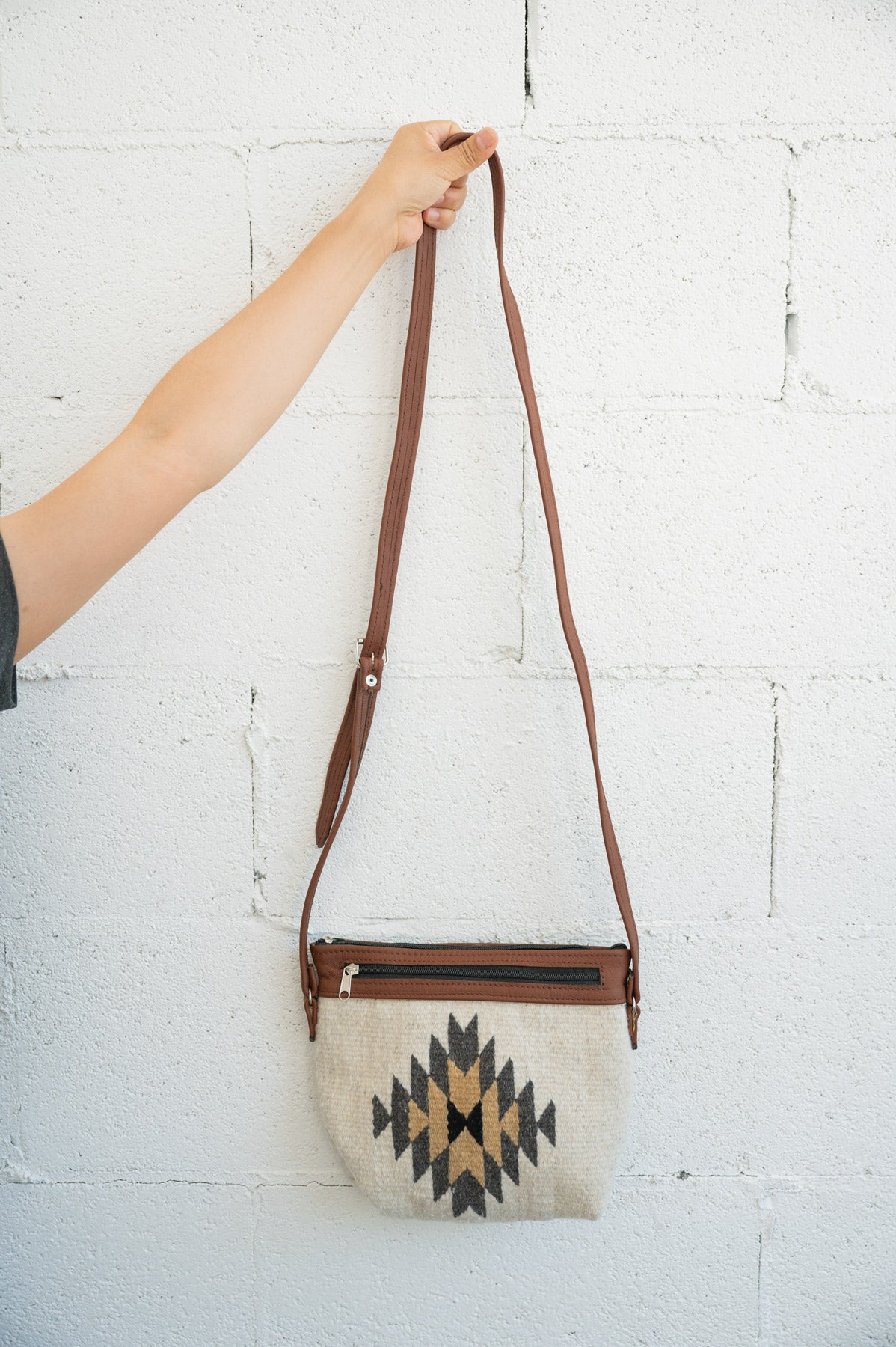 Creme and grey Mexican shoulder bag being held against a white brick wall by an arm