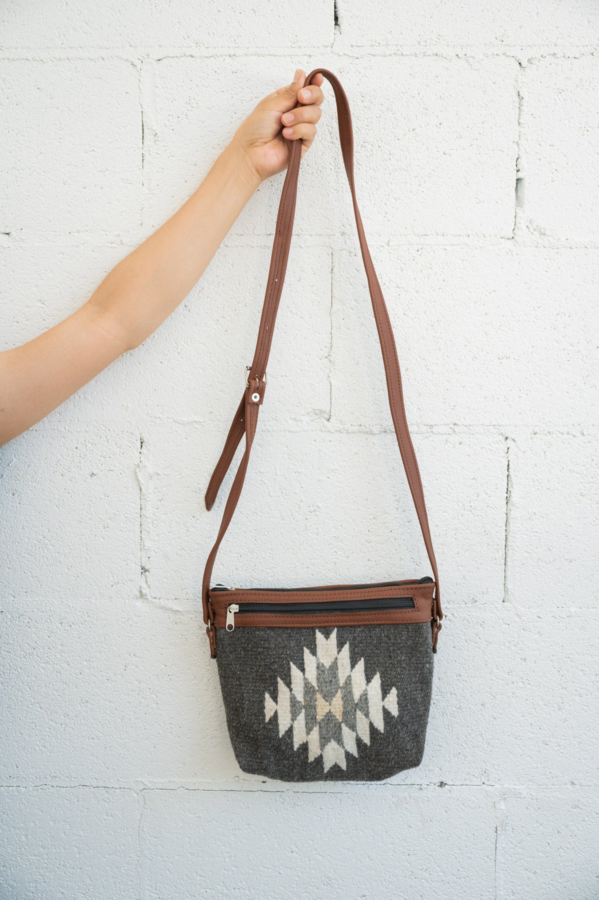 Charcoal and creme Mexican handbag being held against a white brick wall by an arm