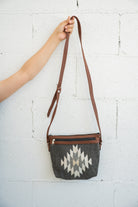 Charcoal and creme Mexican handbag being held against a white brick wall by an arm