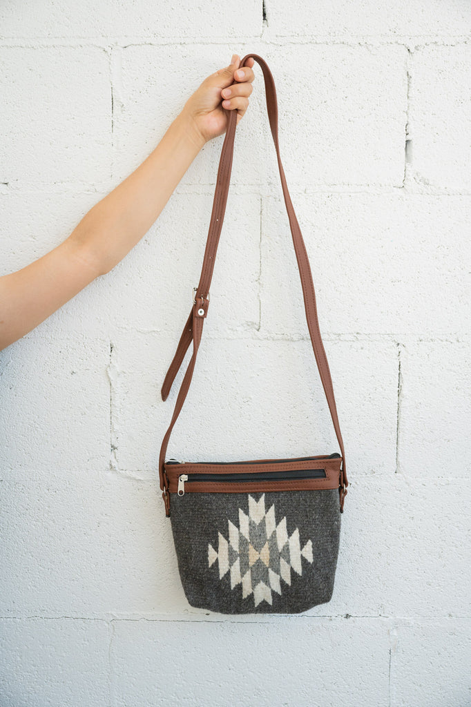 Charcoal and creme Mexican handbag being held against a white brick wall by an arm