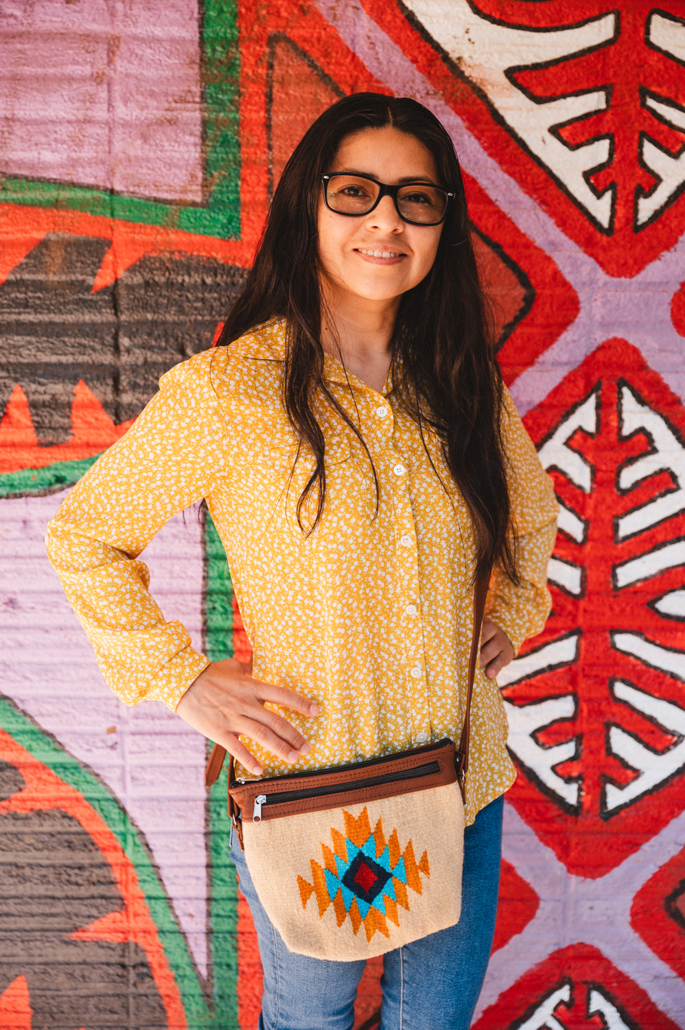 Mexican woman standing in front of colorful wall wearing a handwoven wool purse from teotitlan del valle oaxaca