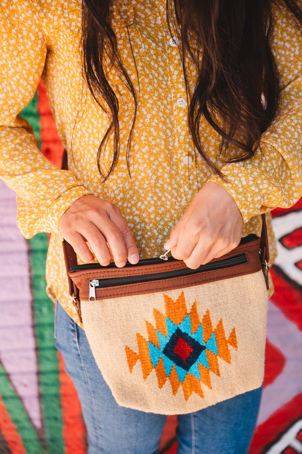 Mexican woman standing in front of colorful wall wearing a handwoven wool purse from teotitlan del valle oaxaca