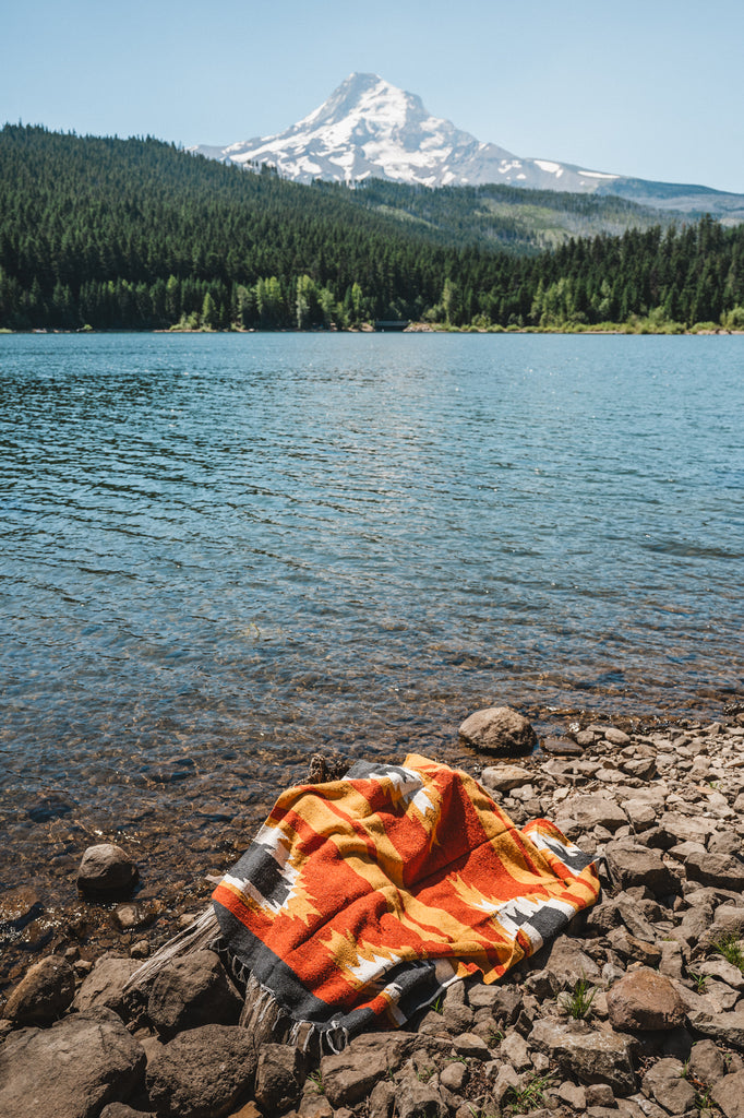 red and yellow zapotec blanket laying on the ground by a lake with mountain view