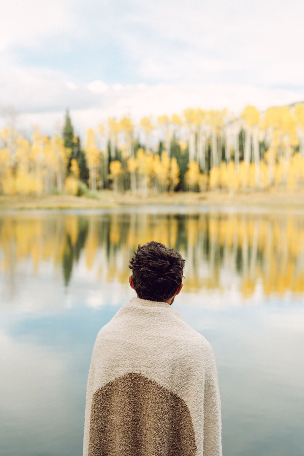 Man wrapped in tan blanket standing in front of a lake