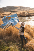 Woman throwing a blue blanket in the air in a field at sunset in the high desert