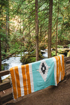 turquoise and gold diamond zapotec blanket laying on a forest fence