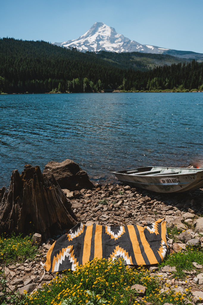 Yellow and black relampago zapotec blanket on ground  in front of mountain lake