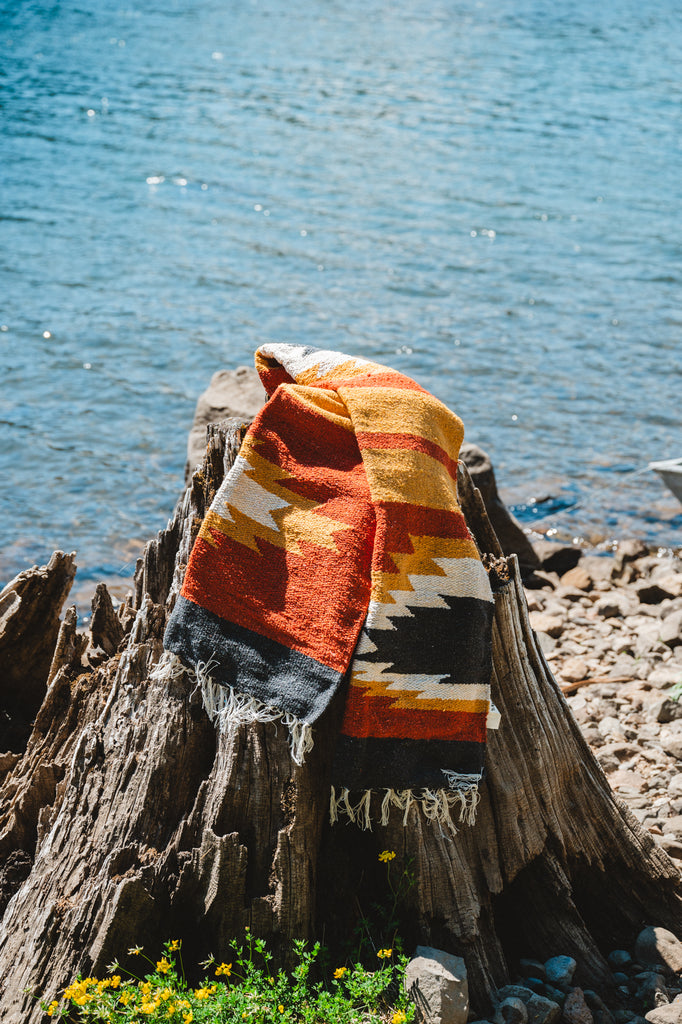 handwoven mexican blanket on a stump by a lake